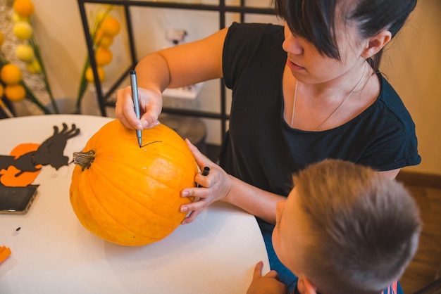 Mother with son making pumpkin head at home together