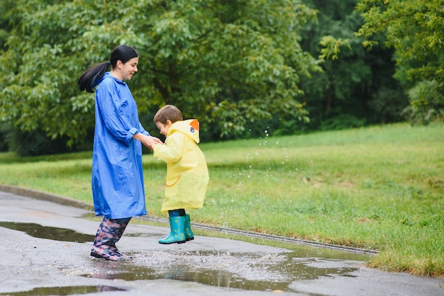 Mother with son walking in the park in the rain wearing rubber boots