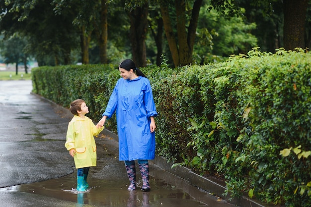 Mother with son walking in park in the rain wearing rubber boots