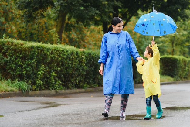 Mother with son walking in park in the rain wearing rubber boots