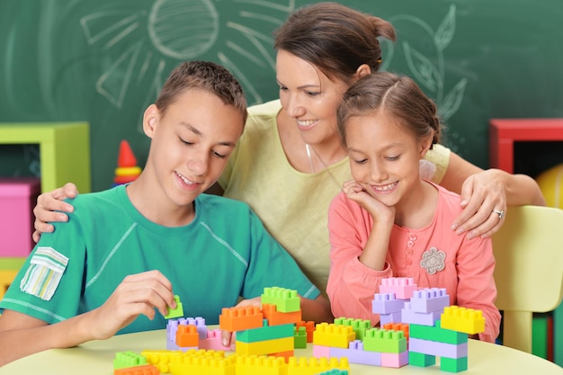 Mother with two children collecting colorful plastic blocks with school blackboard on background