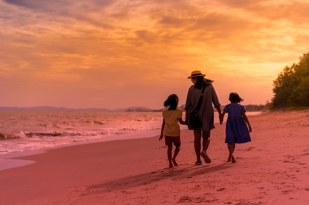 夕日や日の出のビーチで歩いている2人の娘と母