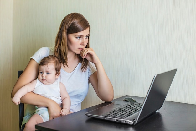 The mother of the woman with the child on hands at work behind the laptop at home