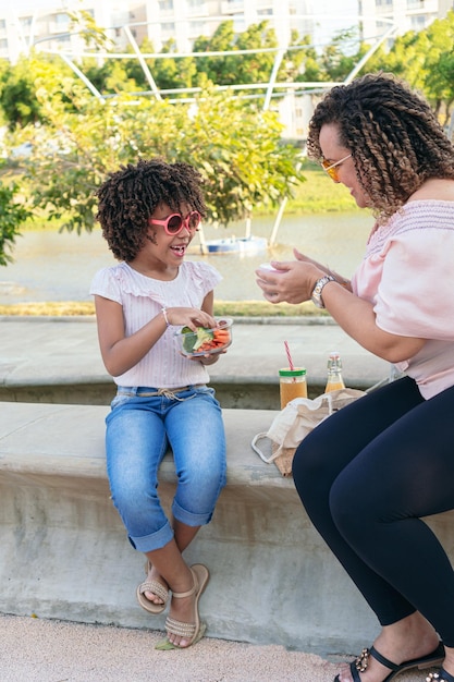 公園で健康的な食べ物を共有する母と若い娘