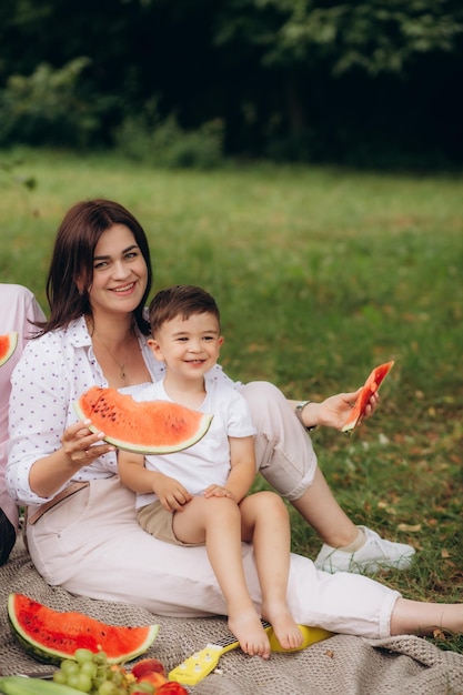 Foto madre e figlio giocavano sull'erba mamma e figlio mangiavano anguria picnic estivo