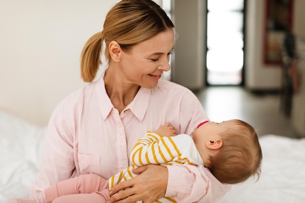 Mother39s care Mom holding her sleeping baby daughter on hands sitting on bed at home caring for her infant girl