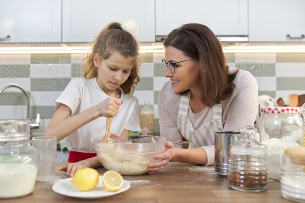 母の日、母と娘の子供が一緒に家庭の台所でクッキーを準備し、ボウルに生地をこねる