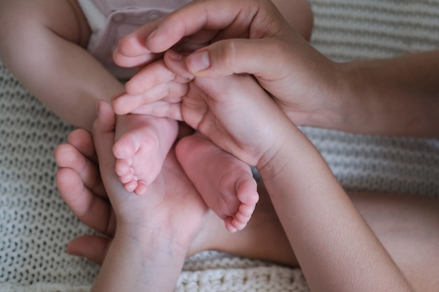 母親の手と子供の手は小さな赤ちゃんのつま先を持っています。 2人の子供と家族。幸せな家族。家で一緒に時間をお楽しみください。スローモーション。愛。甘い。優しさ。