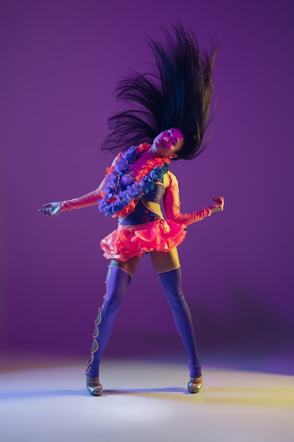 Motion, flying hairs. Hawaiian brunette model on purple studio background in neon light. Beautiful women in traditional clothes smiling and having fun. Bright holiday's, celebration colors, festival.