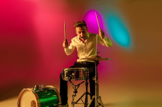 Motion. Young caucasian inspired and expressive musician, drummer performing on multicolored background in neon. Concept of music, hobby, festival, art. Joyful artist, colorful, bright portrait.