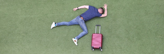 Motionless man lies on green lawn with suitcase