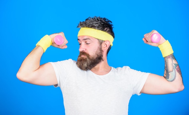 Motivated athlete guy. sportsman training with dumbbells blue background. improve your muscles. man bearded athlete exercising dumbbell. use weights or dumbbells. athlete training with tiny dumbbell