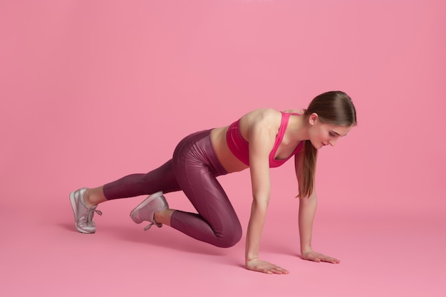 Motivated. Beautiful young female athlete practicing in studio, monochrome pink portrait