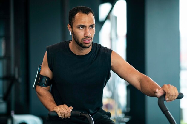 Motivated black man using elliptical bike machine while\
training at gym