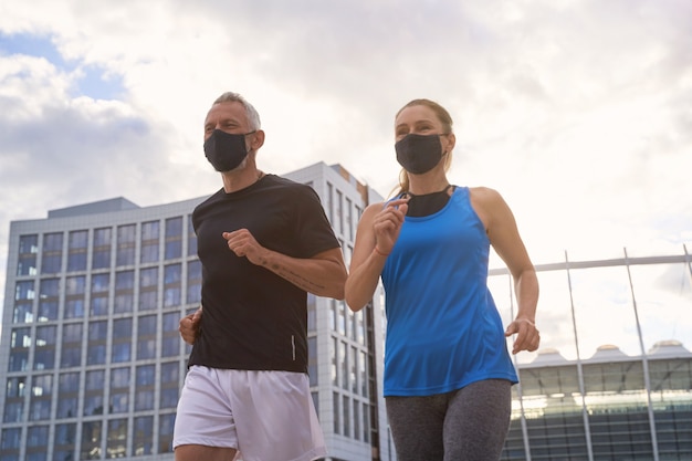 Motivated middle aged couple in protective face masks jogging together in urban environment in the