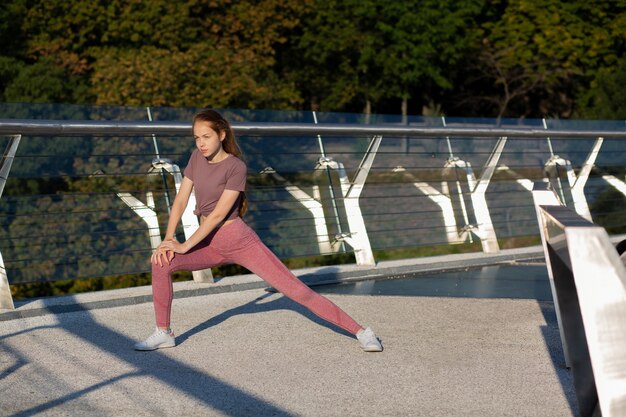 やる気のある赤毛のスポーティーな女性は、橋でのトレーニングの前にウォームアップします。テキスト用のスペース