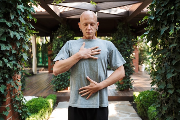 Motivated young fitness man doing breathing exercises while
standing outdoors