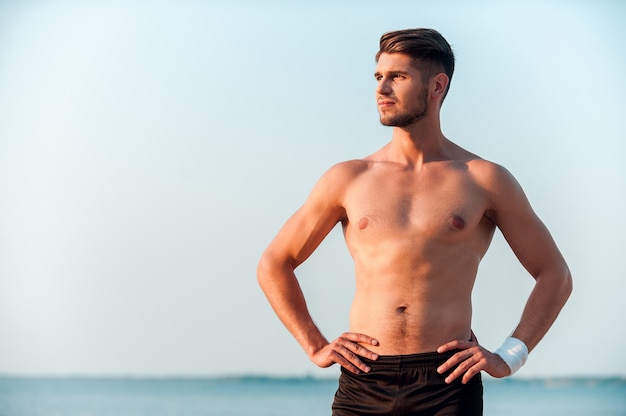 Motivatie brengt me in beweging. Zelfverzekerde jonge gespierde man die handen op de heupen houdt en wegkijkt terwijl hij buiten staat