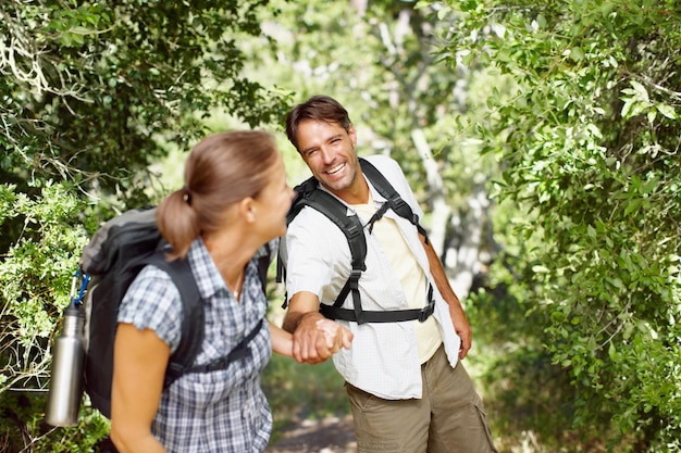 Motivating each other to keep moving A young man being pulled playfully by his wife with backpacks on their backs