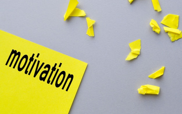 motivation a word written on yellow paper, next to torn shreds on a gray table, the concept of success.