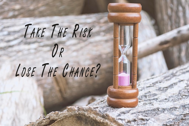 Photo motivational quote with hourglass on tree trunk background take the risk or lose the chance