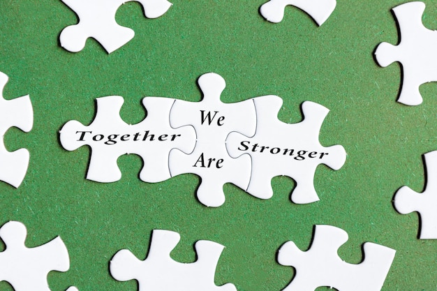 Motivational text on white jigsaw puzzle with green background Together we are stronger