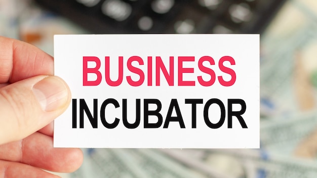 동기 부여 단어 : BUSINESS INCUBATOR. 남자는 BUSINESS INCUBATOR라는 텍스트가있는 종이를 들고 있습니다. 비즈니스 및 금융 개념