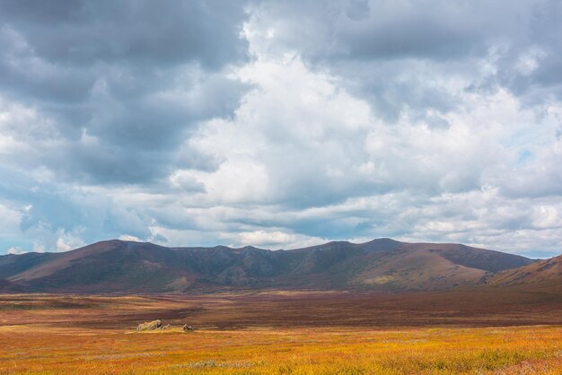 写真 陽光に照らされた高山の高原と山脈の下の劇的な空の麗な秋の色彩 変化する天候における太陽の光と雲の影 晴れと雨