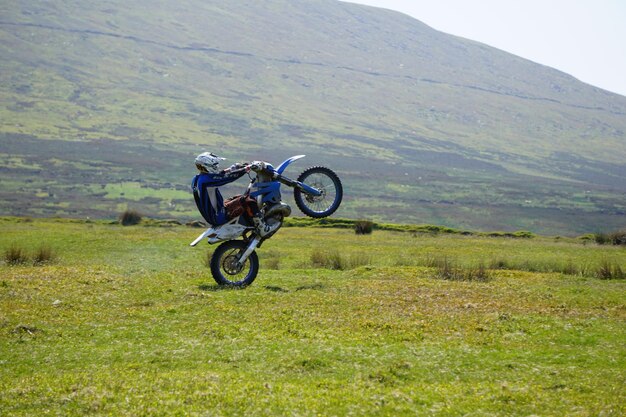 Photo motocross rider performing stunt on field by mountain