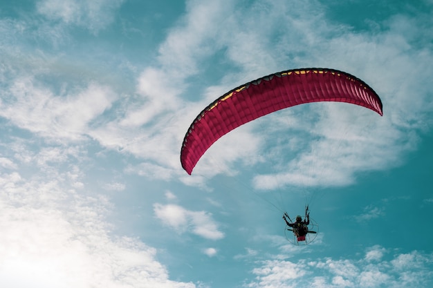 Motor paraglider flying in blue sky with white cloud in background.