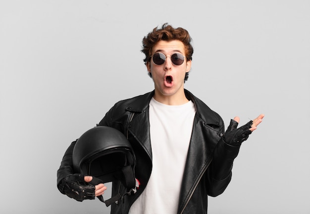 Motorbike rider boy looking surprised and shocked, with jaw dropped holding an object with an open hand on the side