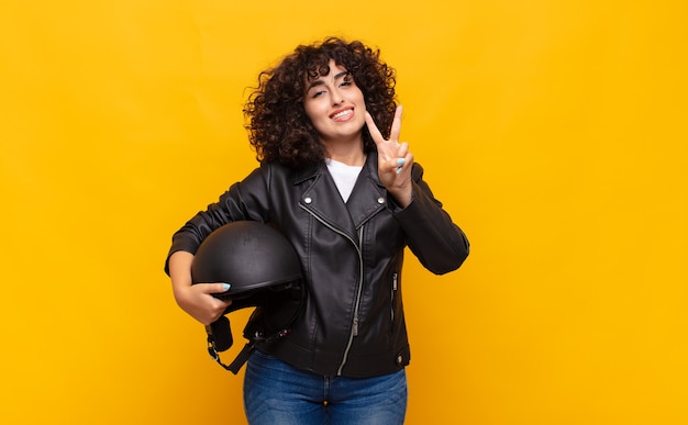 Motociclista donna sorridente e guardando amichevole, mostrando il numero due o secondi con la mano in avanti, conto alla rovescia