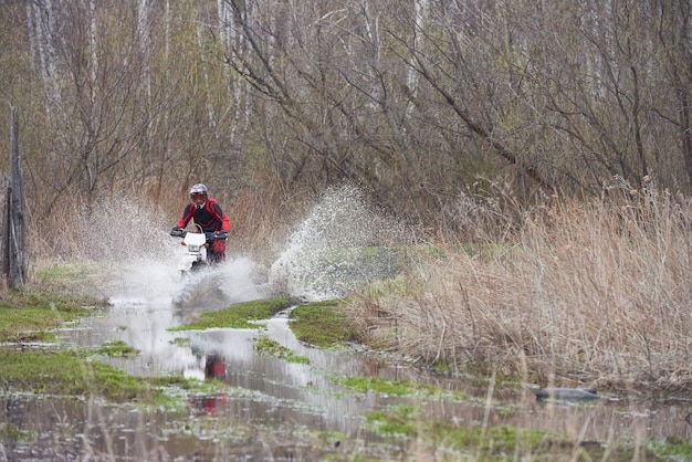 Pilota di motocross che corre nelle pozzanghere durante la competizione in ambiente naturale