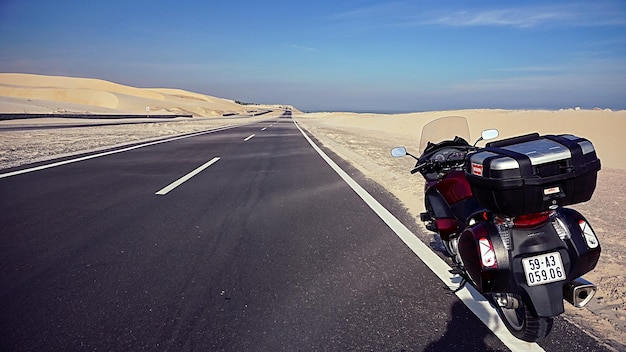 Motorcycle parked on road at desert against blue sky during sunny day