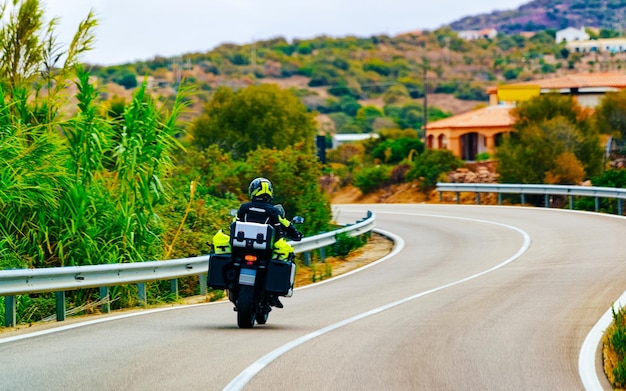 夏にイタリアのサルデーニャ島のコスタスメラルダで道路上のオートバイ。ヨーロッパの高速道路でスクーターを運転するモーターサイクリスト。高速道路で原付の男。オルビア州。ミクストメディア。