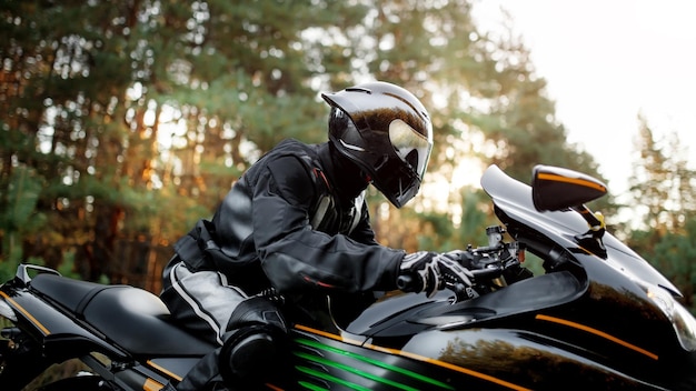 Фото Мотоциклист в шлеме едет по дороге на современном черном мотоцикле. спортивный велосипед. скопируйте место для вашего индивидуального текста. мотоциклист в кожаном защитном снаряжении