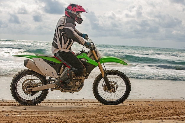 Motorcyclist in a protective suit rides on one wheel of motorcycle on the sea, splashes fly from under the wheels.