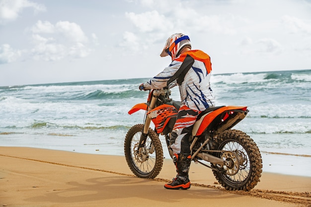 Motociclista in tuta protettiva seduto sulla moto di fronte al mare