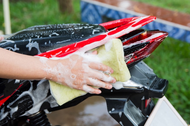 Motorfiets schone, vrouwelijke hand met gele schuimspons die een motorfiets wast.