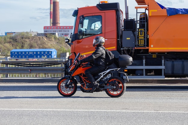 Motorrijder in een helm op een motorfiets op de weg tegen de achtergrond van een oranje vrachtwagen