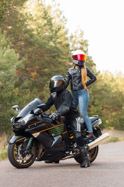 Motorrijder in een leren jas zit op een motorfiets en een meisje staat op een motorfiets in helmen tegen de achtergrond van bomen in het bos