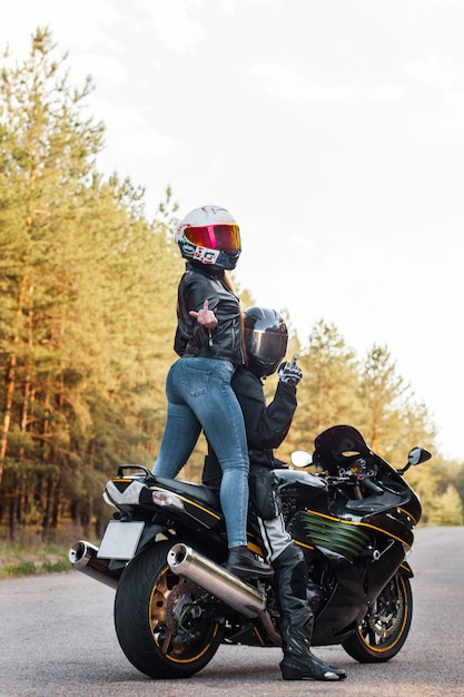 Motorrijder met beschermende uitrusting en helm laat zien hoe hij met middelvinger neukt terwijl hij met een meisje op een motorfiets zit