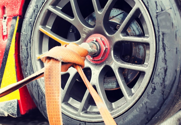 motosports, transportation and racing concept - close up of race car wheel with tow rope tied to it