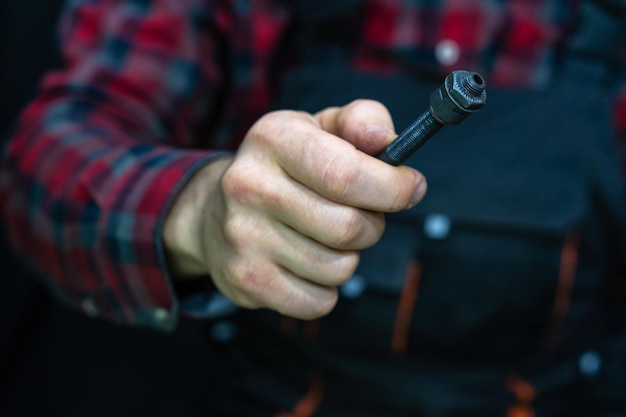 Mountain bike repair Bike mechanic in the workshop Mechanic holds the axle in his hand from the back of the bike bushing Hand and axis closeup A man in a fashionable plaid shirt