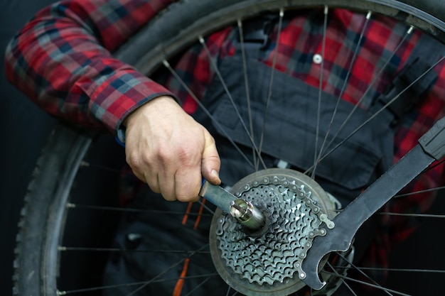 マウンテンバイクの修理ワークショップでの自転車整備士後輪カセットの交換汚れたホイールハブとスポーク、摩耗した折りたたみ式タイヤ自転車で作業するためのプロフェッショナルツール