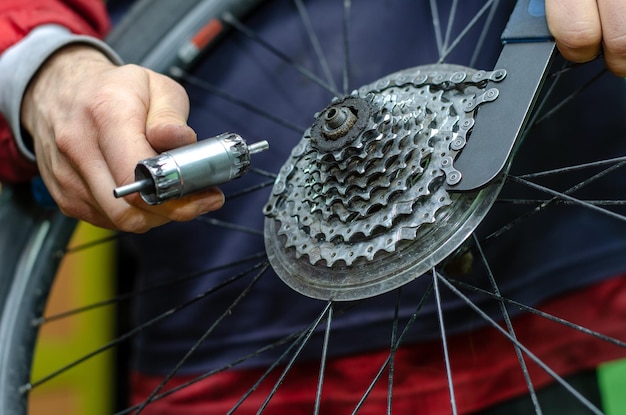 산악 자전거 수리 마스터는 카세트 스프로킷 리무버 체인 채찍을 제거하기 위한 도구를 손에 들고 있습니다.