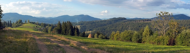 Mountain evening panorama view with earth road, haystackes and country estate (Slavske village outskirts, Carpathian Mts, Ukraine). Nine shots composite picture.