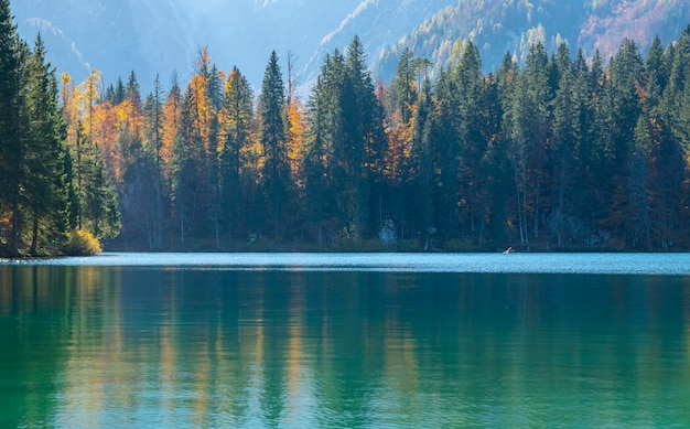 Mountain lake, autumn trees and mighty mountains in sunlight