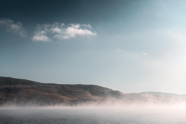 Mountain lake in foggy morning Blue sky with clouds and fog over the water