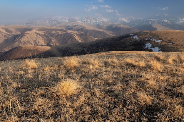 Mountain landscape with tufts of dry grass on a hillside and snowcapped peaks Caucasus Russia